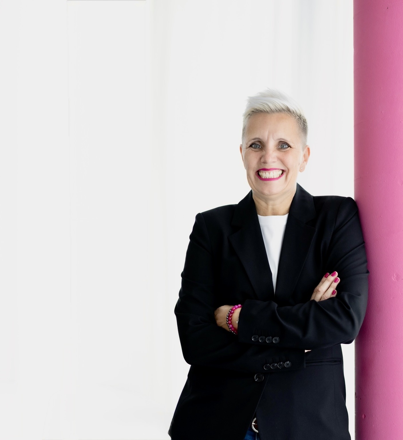 Rechtsanwältin, DSGVO-Expertin Christiane Henneken mit verschränkten Armen an eine eine pinkfarbene Säule gelehnt. Sie lacht offen. Sie trägt einen schwarzen Blazer und ein weißes T-Shirt.